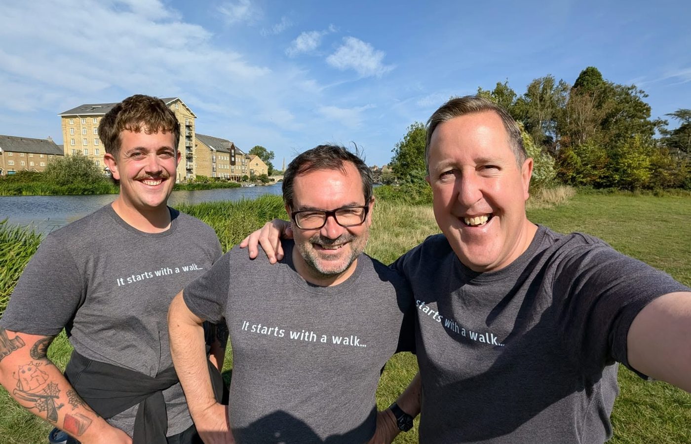 Three men in It starts with a walk t-shirts by the river at St Ives.